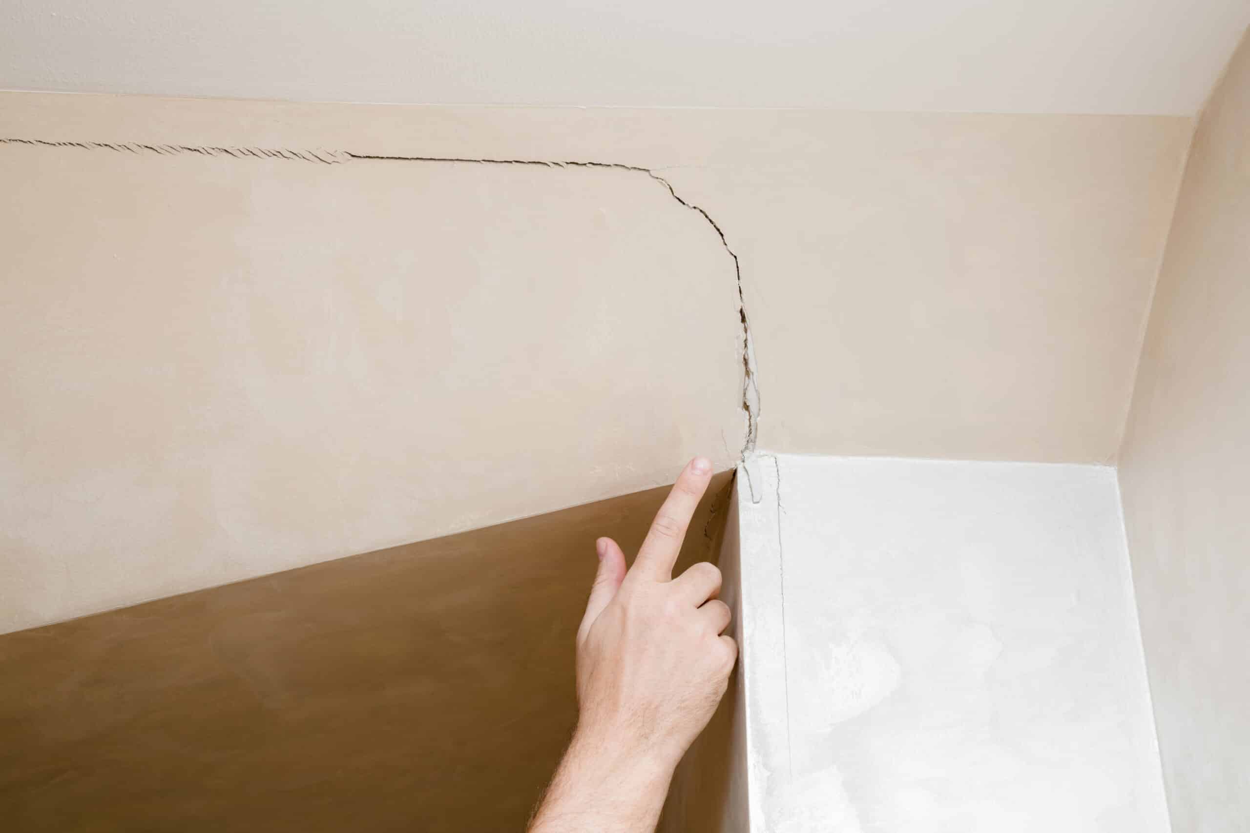 man's hand finger pointing to the cracked wall in house. buildin