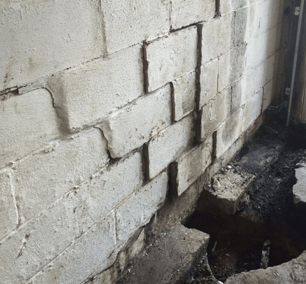 Cracked and shifting concrete block basement wall with damaged footing below