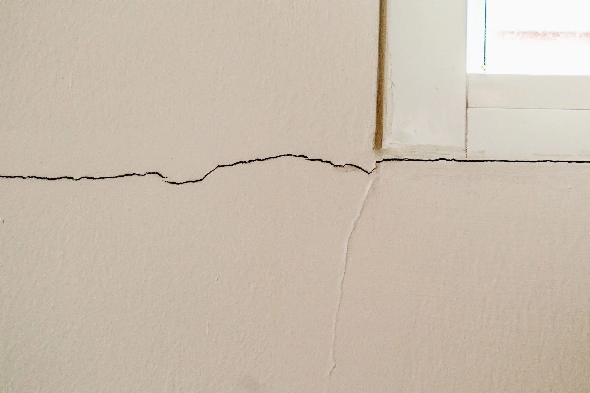 Horizontal and vertical cracks meeting near a window corner from foundation shifting