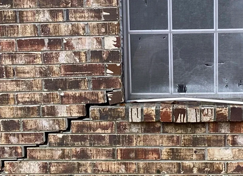 Stair-step crack in exterior brick wall beneath a window signaling foundation settlement
